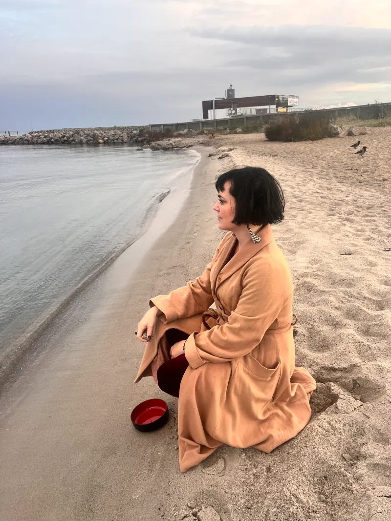 Julie sidder ved vandkanten på en strand